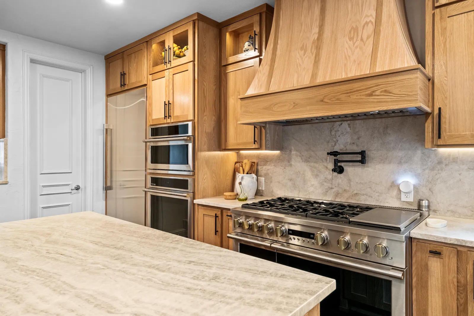 Taj Mahal quartzite counters and full-height slab backsplash behind a professional range in Plano, TX
