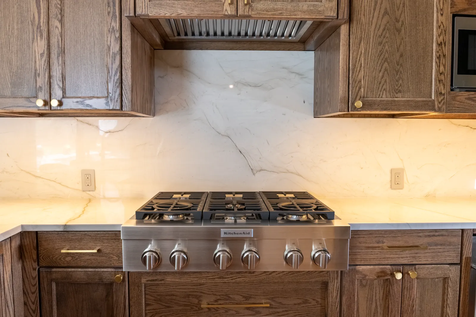 Marble slab backsplash behind a gas range with oak cabinetry in a Preston Hollow, Dallas kitchen